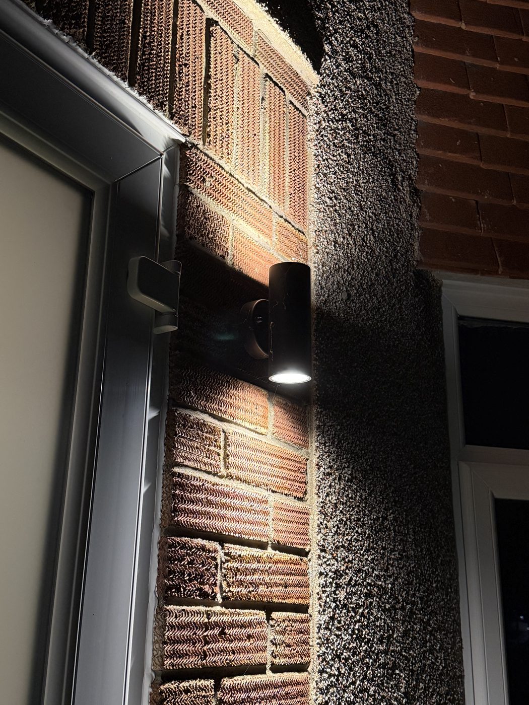 An outdoor wall light lit on a brick wall at night
